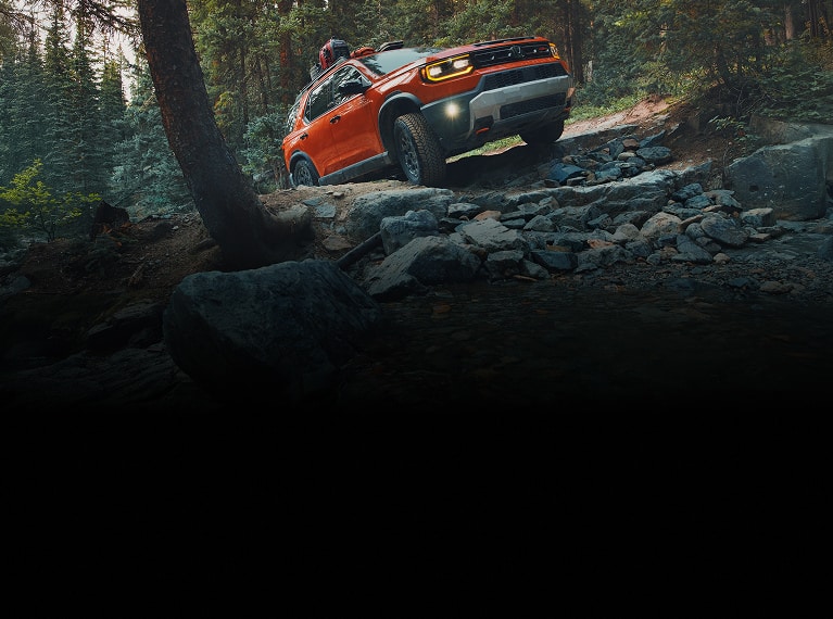 2026 Honda Passport TrailSport Elite in Sunset Orange front off-roading on a rugged rocky forest trail (Mid-Size SUV).